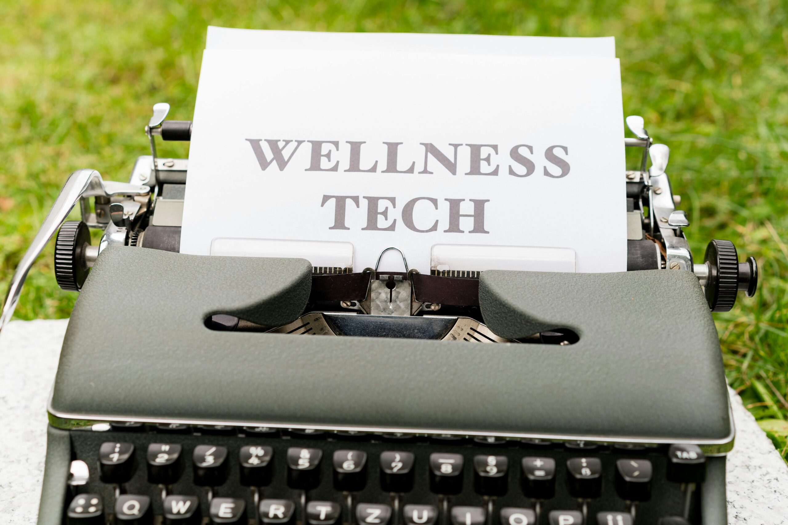 A retro typewriter outdoors displaying a 'Wellness Tech' message on paper.